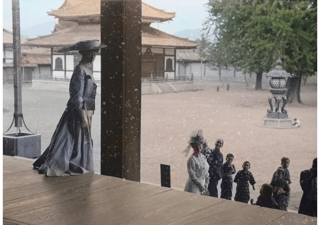 日本奥地紀行の表紙 — 明治初期、寺院の縁側に立つ洋装の婦人と日本人（手彩色写真）